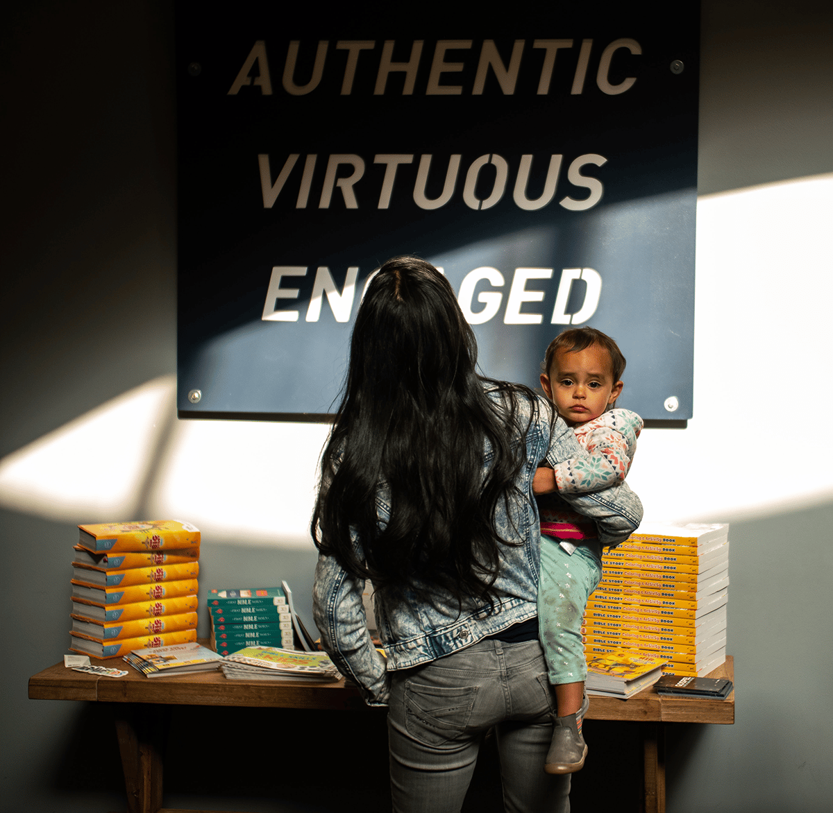 woman holding child in front of a sign that says authentic virtuous engaged