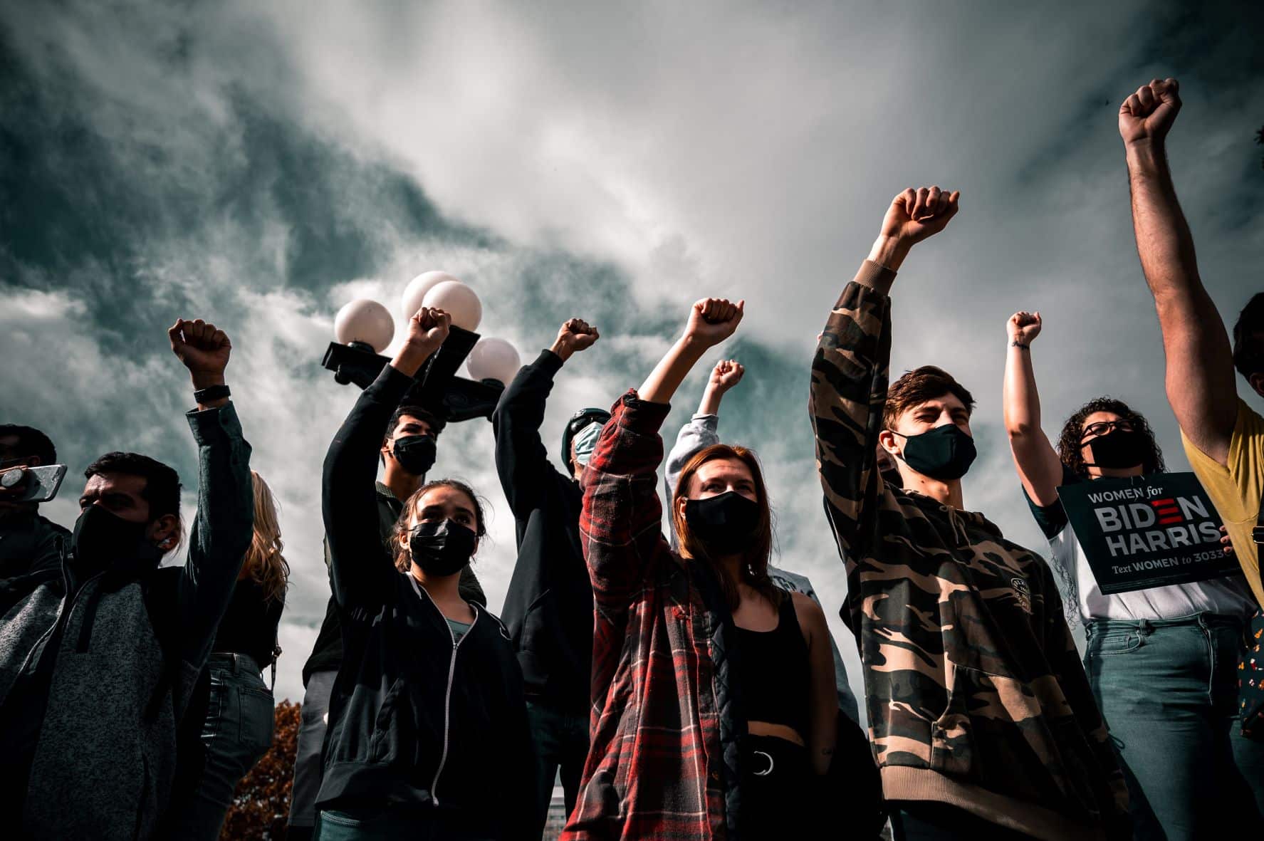 group of people with masks holding political signs and raising their fists in the air