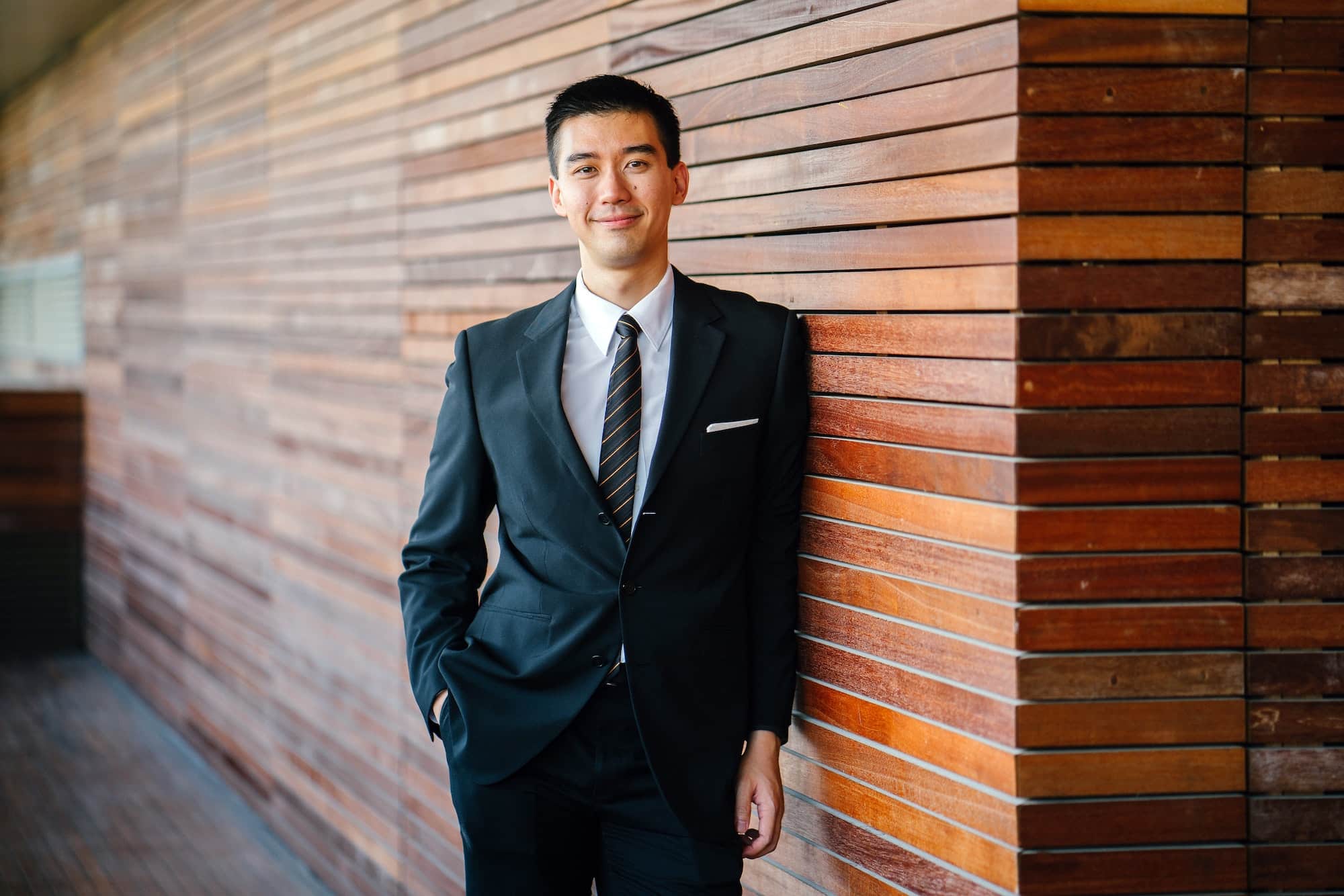 man in suit leaning up against modern wooden wall