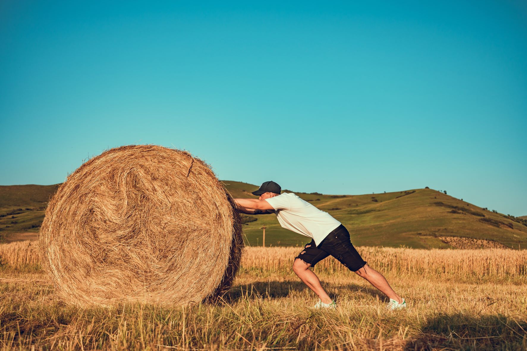 man pushing on large haystacks