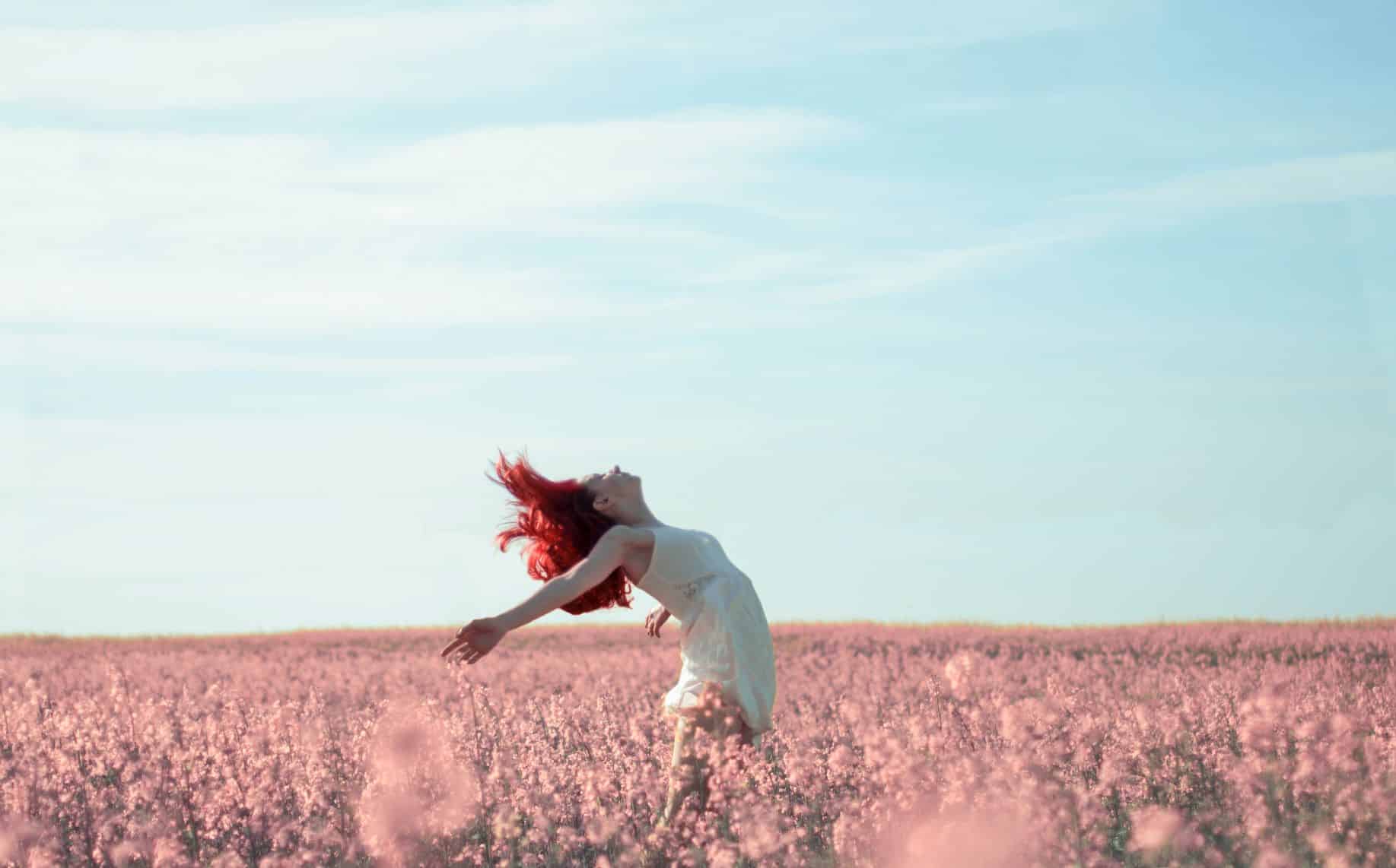 red haired woman throwing arms back in large pink field