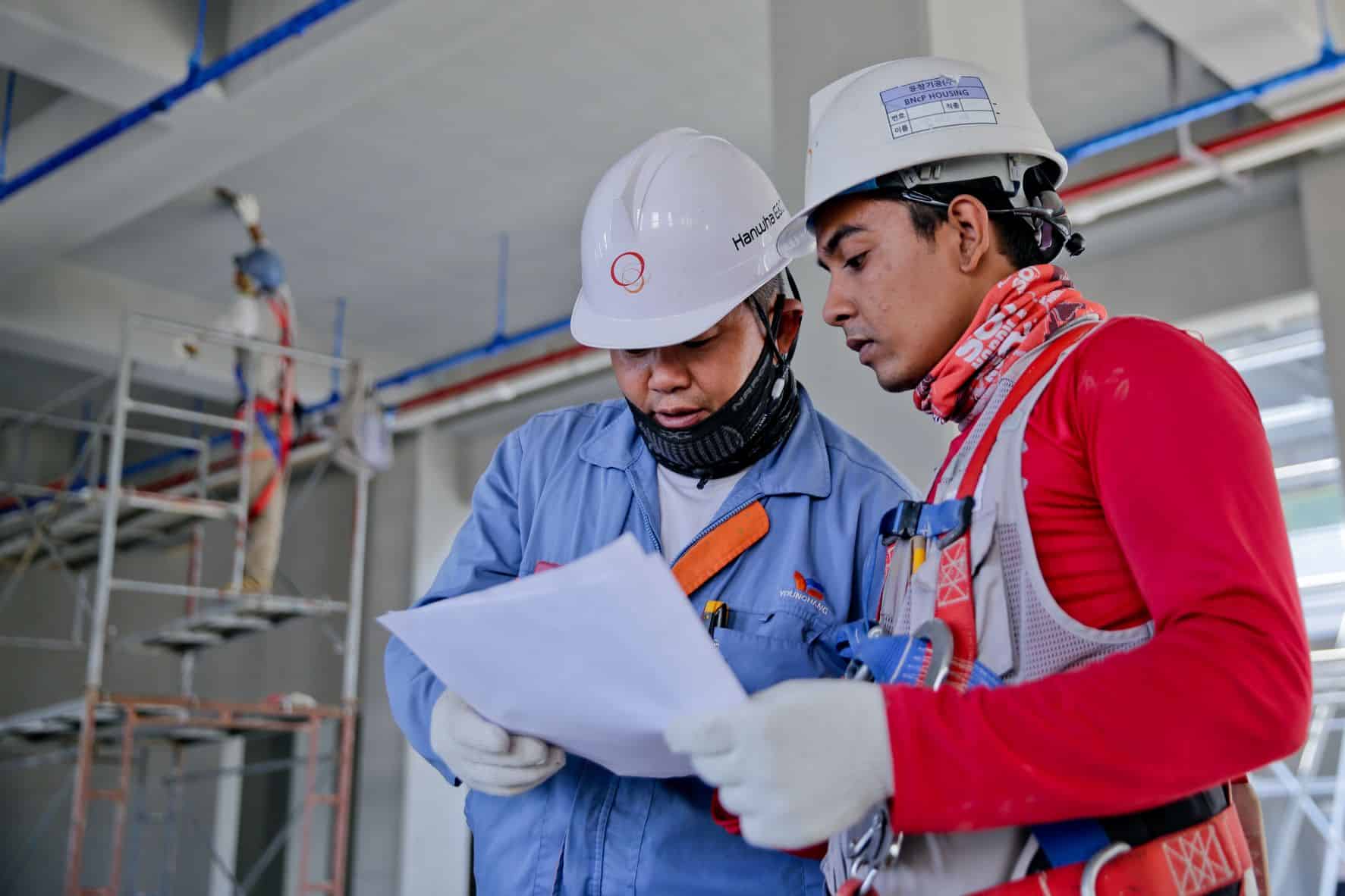 two people in hard hats looking over documents